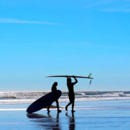 0002_man-and-womans-silhouette-on-blue-background-beach-with-surf-boards-getting-ready-to-go-surfing_t20_9JVrZY